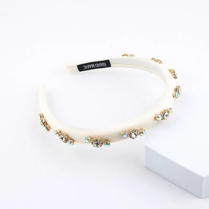 Handmade cream sponge headband with sparkling rhinestones on a minimalist white stand