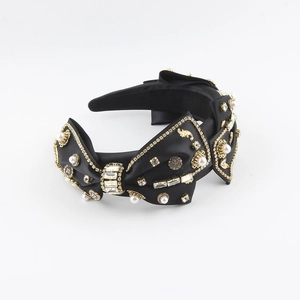 Detailed macro view of black satin headband with gold baroque bow and sparkling rhinestones