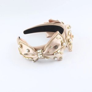 Detailed view of champagne satin headband with pearls, rhinestones, and metal accents