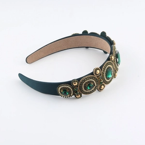 Detailed view of hand-beaded emerald gems and gold beads on a velvet baroque headband