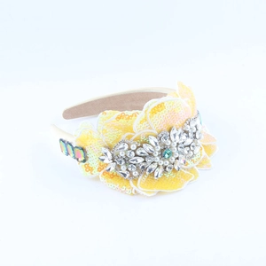 Detailed close-up of yellow sequin floral headband with crystals and pearls on white base