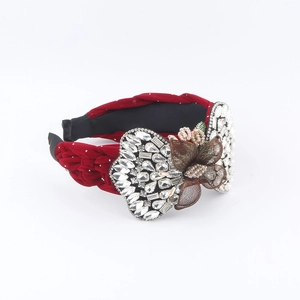 Détail d'un serre-tête en velours rouge torsadé avec ailes en strass et fleur