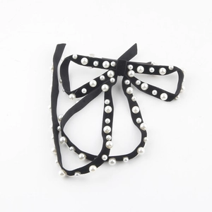 Detailed macro view of black velvet bow hair clip featuring elegant faux pearl accents