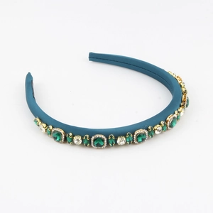 Detail of blue satin padded headband with emerald green and clear gemstones on gold alloy