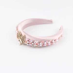 Gros plan du serre-tête en satin rose orné d'un papillon doré et de cristaux brillants