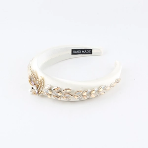 Détail du serre-tête en satin blanc avec vigne en strass et nœud doré élégant