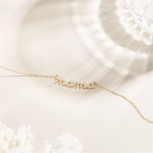 Elegante bracciale MAMA placcato oro 14k con pietre di zircone scintillanti su sfondo crema