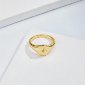 Detalle de un anillo de sello dorado con grabado de estrella y una única piedra de circón