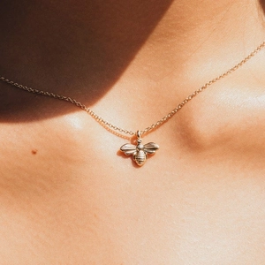 Gros plan d'un collier pendentif abeille doré sur une femme avec jeu d'ombres