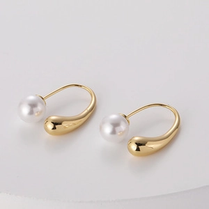 Detail of drop-shaped gold earrings with white pearls in a minimalist U-shaped design