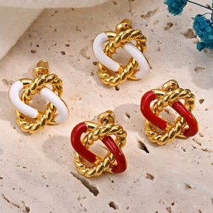 Details von gedrehten Goldcreolen mit weißem und rotem Emaille-Finish auf Steinfläche