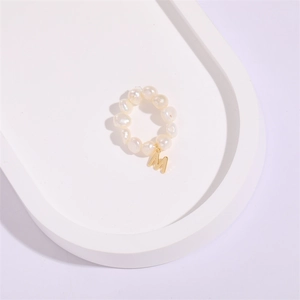 Baroque pearl ring featuring a dangling gold metal letter M pendant on a white tray