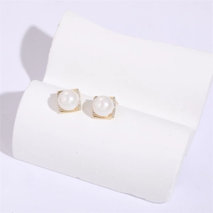 Macro shot of square gold pearl stud earrings with zircon accents on a white stone base