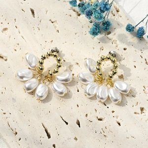 Detailed shot of gold fan-shaped pearl earrings on a beige textured stone background
