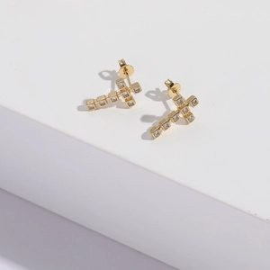 Vue rapprochée de boucles d'oreilles croix dorées serties de zircons sur pierre blanche