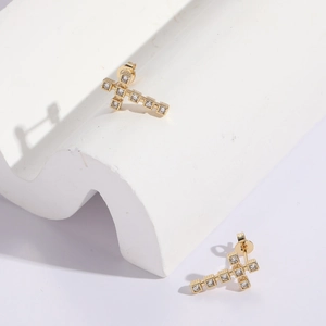 Boucles d'oreilles croix dorées avec zircons étincelants sur des socles blancs purs