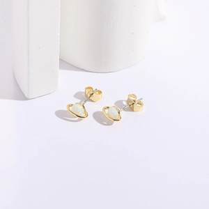 Detailed close-up of golden Saturn stud earrings with white opal stones on white props