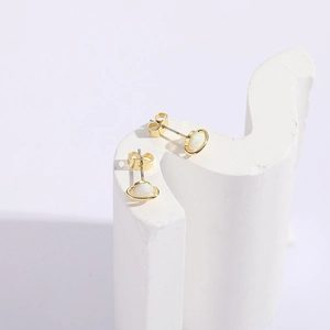 Detail view of golden Saturn-shaped stud earrings with white opal stones on a white stand