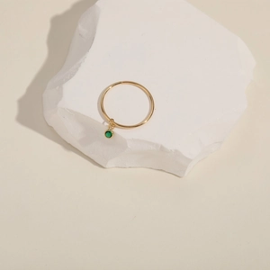 Close-up of gold ring with a round green gemstone pendant on a white textured stone