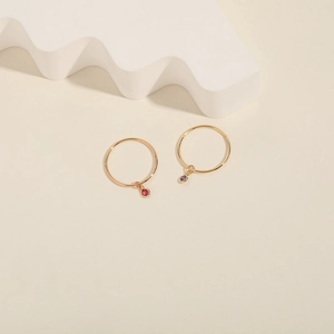 Detail of gold hoop earrings featuring elegant red and purple gemstone charms on a pedestal