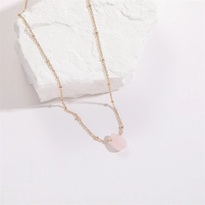 Minimalist gold beaded necklace with pink teardrop crystal pendant on white stone