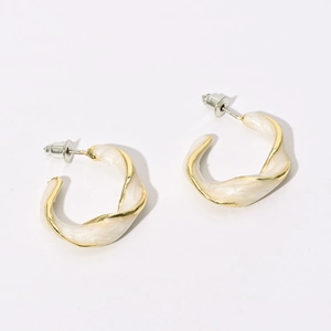 Macro detail of twisted C-shaped hoop earrings with cream enamel and gold finish