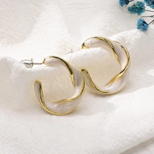 Detail view of C-shaped twisted gold earrings with white enamel marble on linen fabric