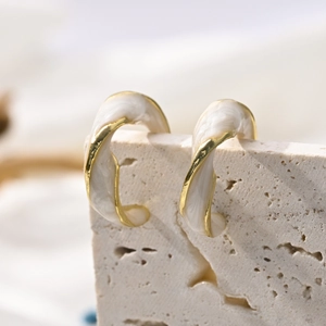 Close-up of C-shaped gold twisted earrings with white marble enamel on a stone base