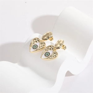 Golden heart-shaped evil eye drop earrings with hammered texture and white enamel details