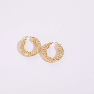 Close-up detail of golden twisted hoop earrings with textured braided metal surface