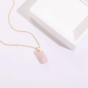 Collier doré minimaliste avec pendentif cylindrique en quartz rose sur socle blanc
