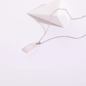 Pendentif cylindrique minimaliste en quartz rose et chaîne argentée sur fond blanc pur