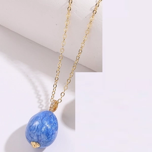 Macro shot of an enamel egg pendant with blue marble texture and 14K gold-plated chain