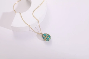 Detailed macro view of Fabergé style gold egg pendant with teal enamel and zircons