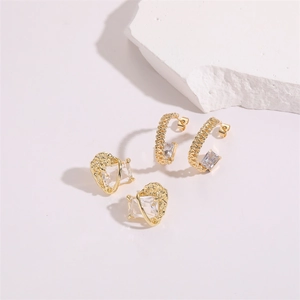 Détail de boucles d'oreilles dorées martelées en C avec zircons sur des pierres blanches