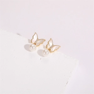 Close-up of golden butterfly earrings with shell wings, zircons, and round pearls