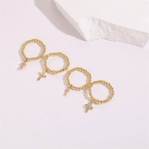 Detail of four-piece gold beaded elastic rings with zircon cross charms on white stone