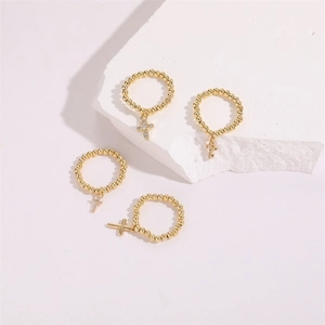 Set of four 14K gold plated beaded rings with zircon cross pendants on stone display