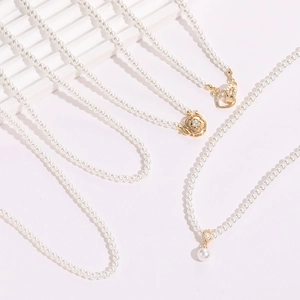 Détail de collier de perles avec pendentif rose dorée et breloques cœur en zircon sur blanc