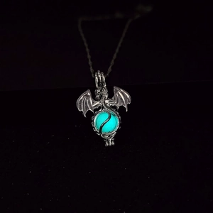 Detailed close-up of a glowing blue dragon pendant with silver wings on black background