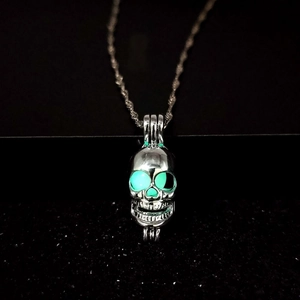 Close-up of silver skull pendant with luminous green glowing eyes on a dark background