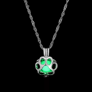 Detailed view of silver claw pendant necklace with glowing green bead on black background