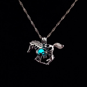 Close-up of a hollow horse pendant with a glowing blue bead on a black background