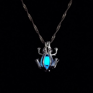 Detail shot of glowing blue frog pendant necklace with silver finish on black background