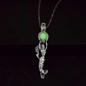 Detailed view of mermaid pendant with luminous green bead glowing in silver cage