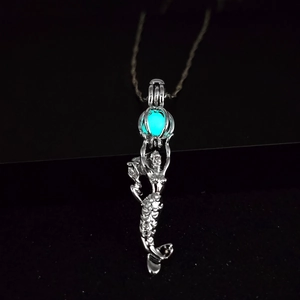 Macro detail of mermaid pendant with glowing teal luminous stone on a dark background