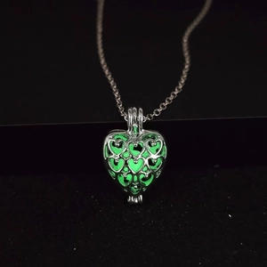 Détail d'un pendentif cœur ajouré avec une pierre lumineuse verte brillante la nuit