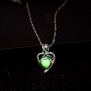 Macro shot of luminous heart pendant necklace glowing green on a dark background