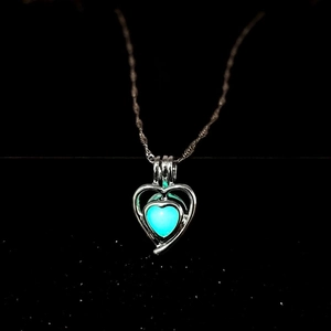 Detailed macro of a hollow heart pendant with glowing cyan stone on a fine silver chain