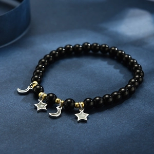 Detail eines Perlenarmbands mit schwarzen Onyxsteinen und silbernen Stern-Mond-Anhängern